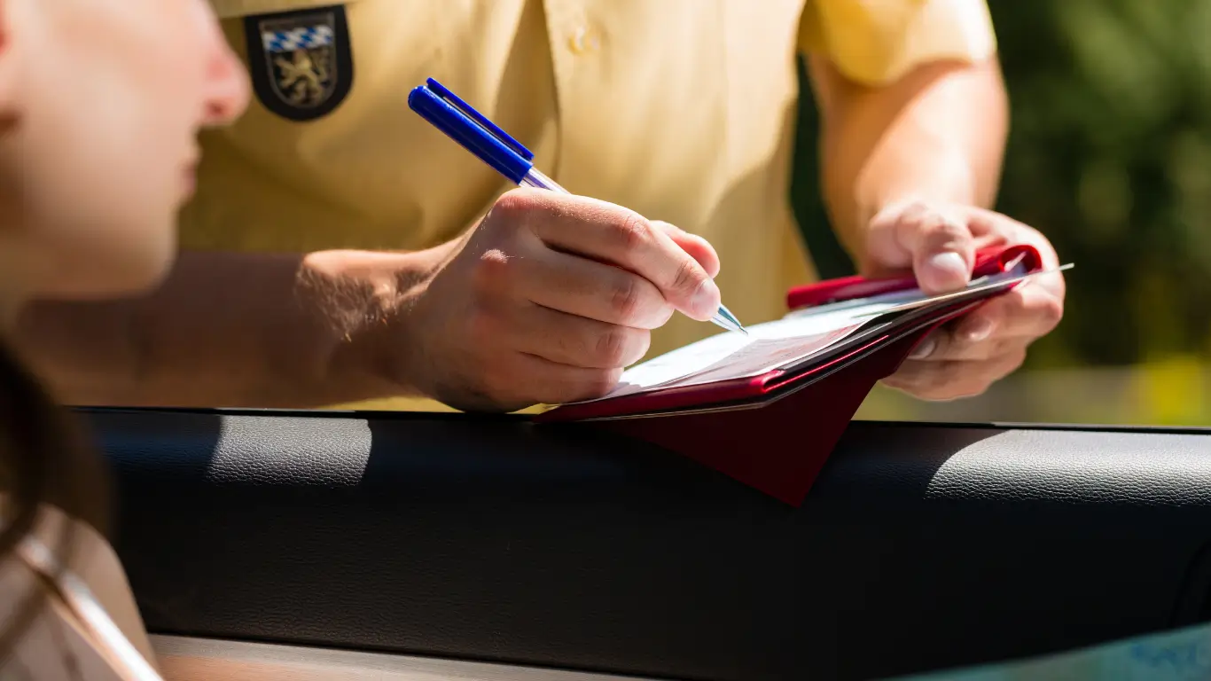 Officer writing a traffic ticket on a clipboard during a roadside stop.