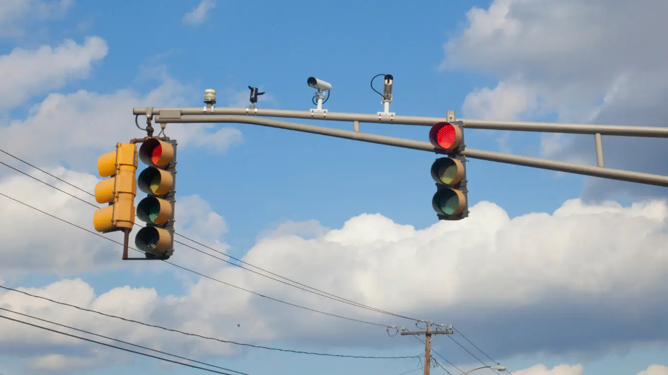 Traffic lights with red signals and mounted red light cameras at an intersection.