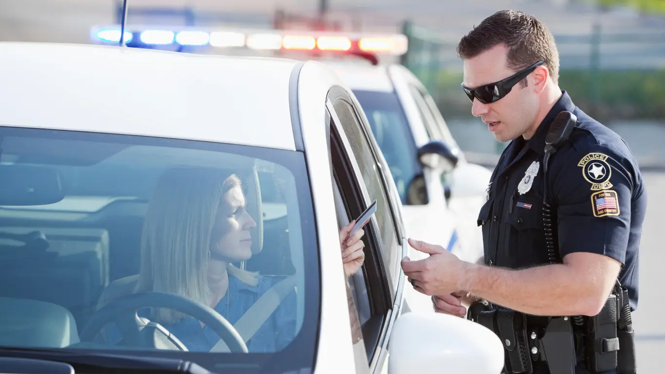 Police officer speaking with a driver during a roadside traffic stop with patrol lights in the background.